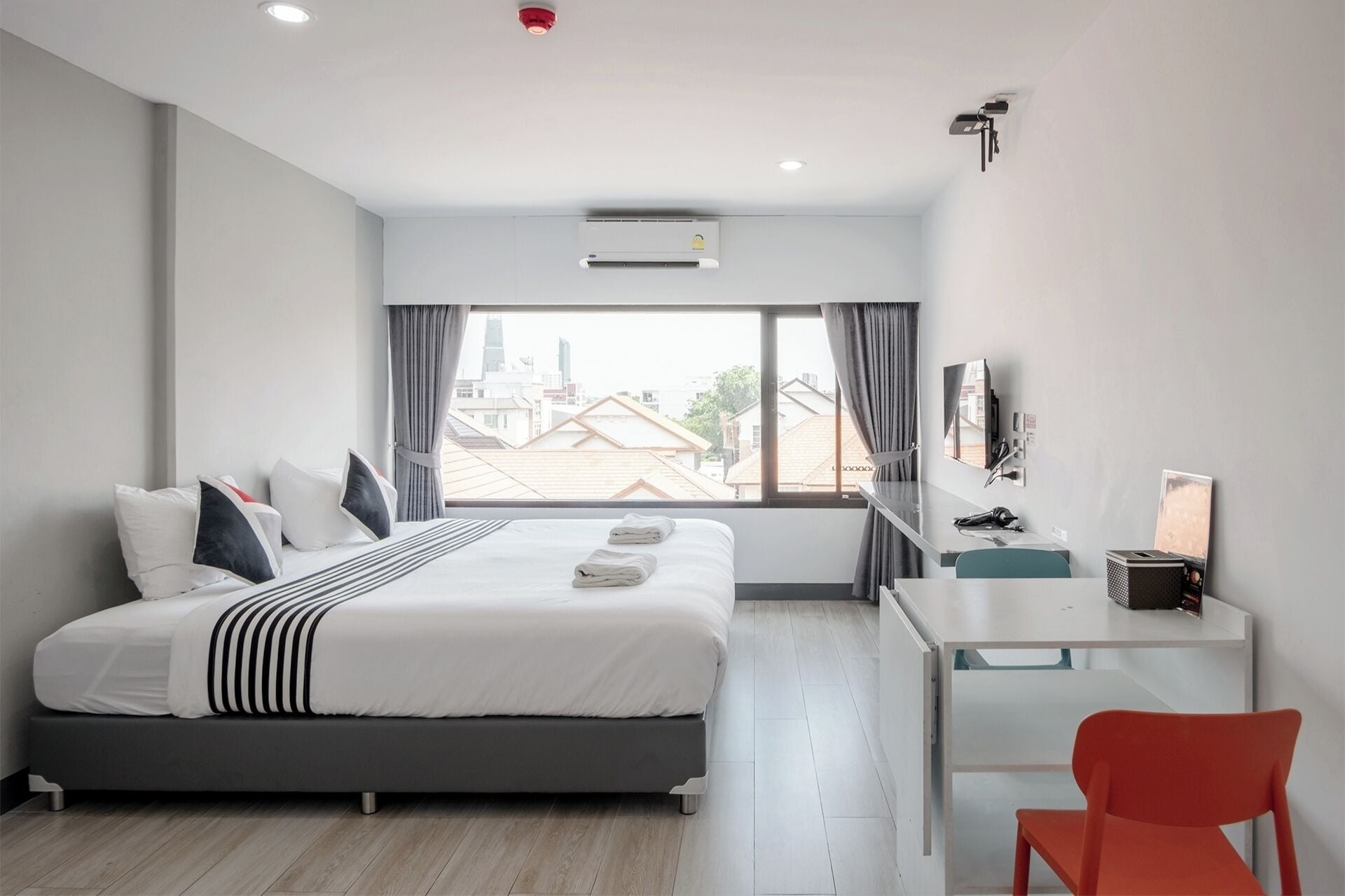A modern hotel room with a large bed, a desk, a chair, and a TV.