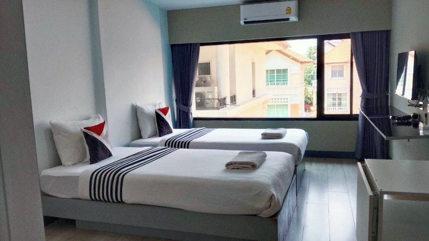 A hotel room with two beds, a desk, and a window with curtains.