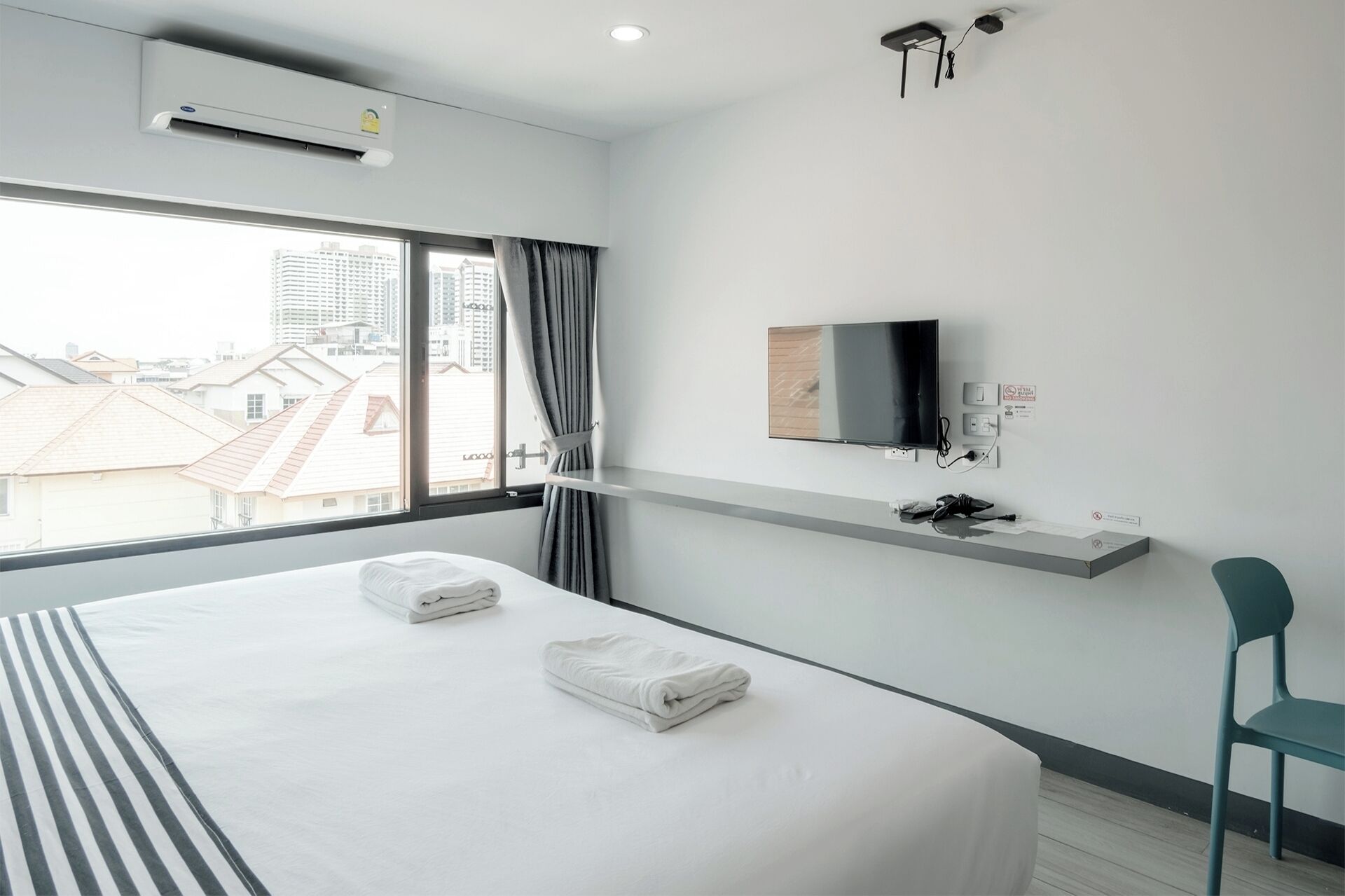 A modern hotel room with a large bed, a mounted TV, and a view of city buildings through the window.