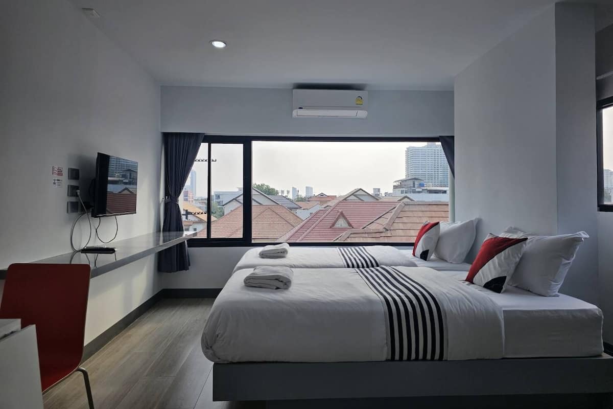 A modern hotel room with a large bed, a TV mounted on the wall, and a view of the cityscape through a large window.