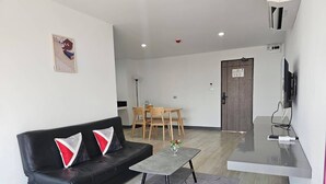 A modern living room with a black leather sofa, a small round table, and a dining area with wooden chairs. - Area Place Hotel (Bangkok)