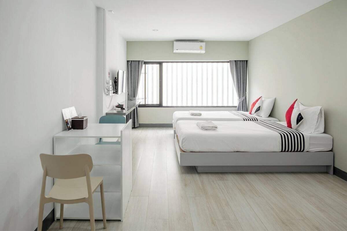 A hotel room with a bed, a desk, a chair, and a window with curtains.