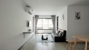 A modern living room with a sofa, a dining table, and a large window. - Area Place Hotel (Bangkok)