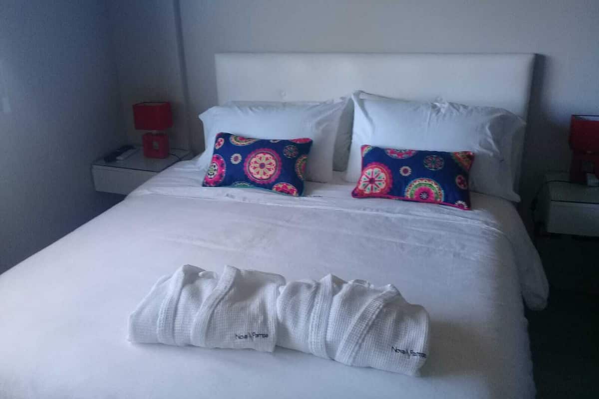 A hotel room with a neatly made bed, two pillows with a colorful pattern, and a pair of white towels on the bed.