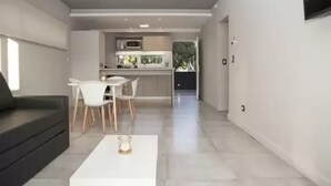A modern living room with a sofa, a dining table with chairs, and a kitchen area in the background. - Nova Pampa apart&spa (Mar Azul)