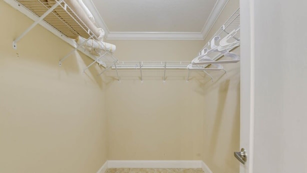 A small, enclosed walk-in closet with beige walls and tiled flooring. It features a metal rack with hanging clothes and a white door. - Loggerhead Lagoon - Waterfront & Pet Friendly (Sugarloaf Key)
