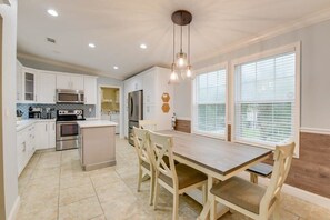 A modern kitchen with white cabinets, stainless steel appliances, and a wooden dining table.