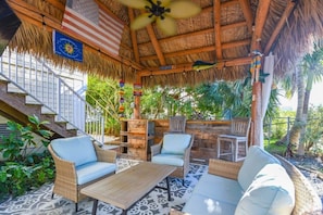 A covered outdoor seating area with wicker furniture, a ceiling fan, and a flag.