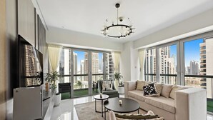 A modern living room with a sofa, coffee table, and TV. Large windows offer a view of tall buildings.