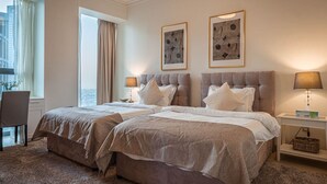 A hotel room with two beds, a desk, and a chair. There are two framed artworks on the wall.
