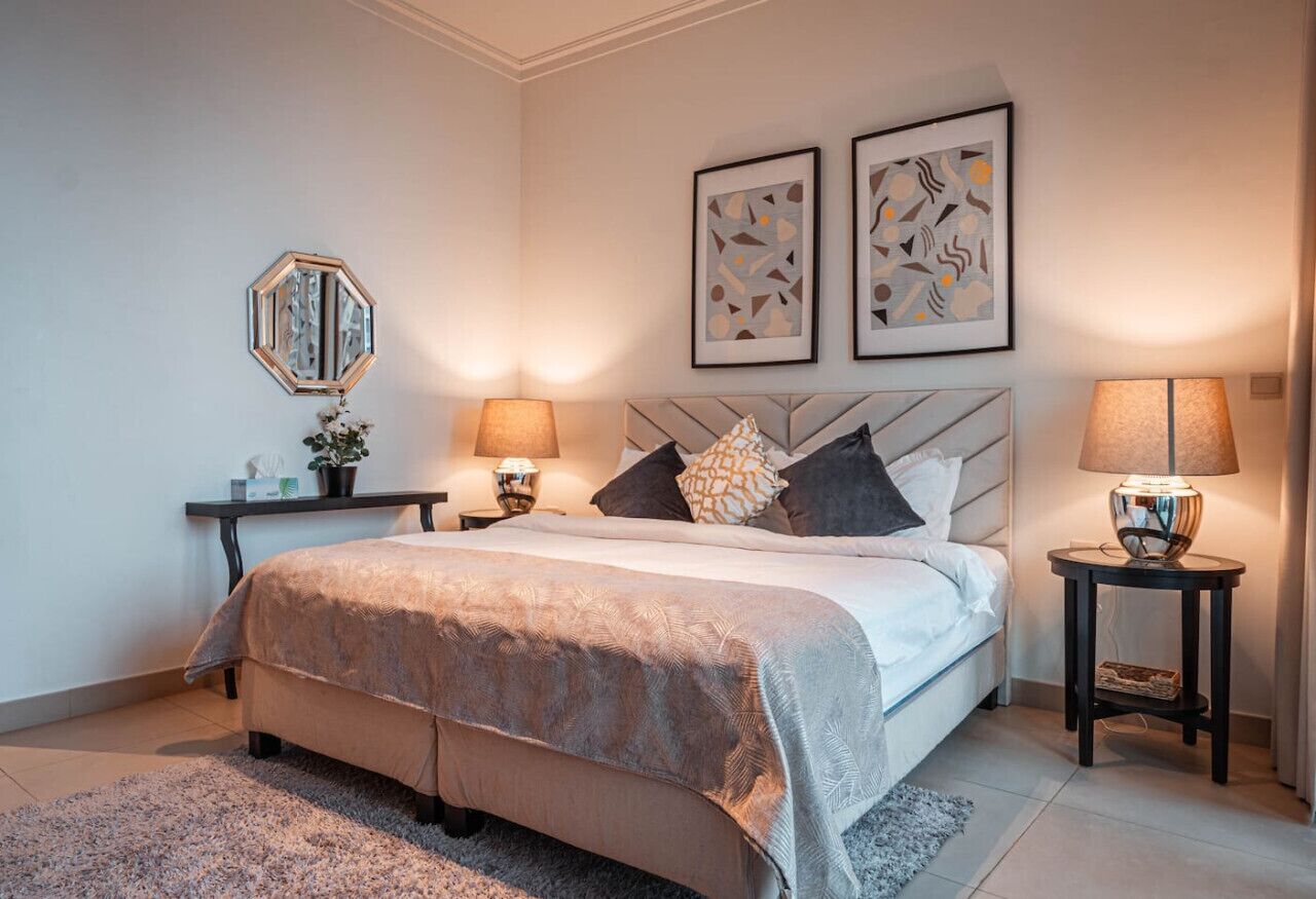 A bedroom with a bed, two bedside tables, a nightstand, a mirror, and abstract wall art.