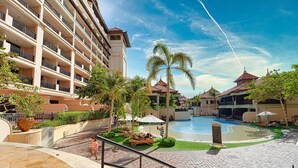 A hotel with a swimming pool, palm trees, and a multi-story building with balconies.