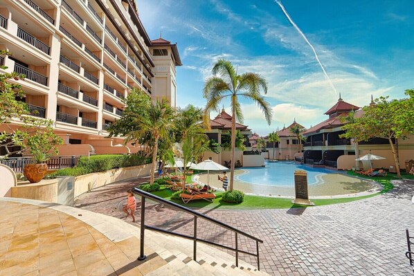 A hotel with a swimming pool, palm trees, and a multi-story building with balconies.