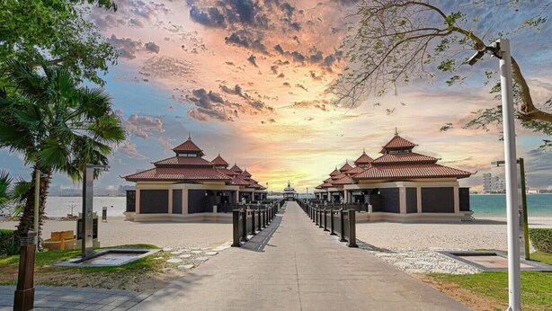 A pathway leading to traditional-style pavilions with a view of the sea and a sunset.