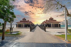 A pathway leading to traditional-style pavilions with a view of the sea and a sunset.