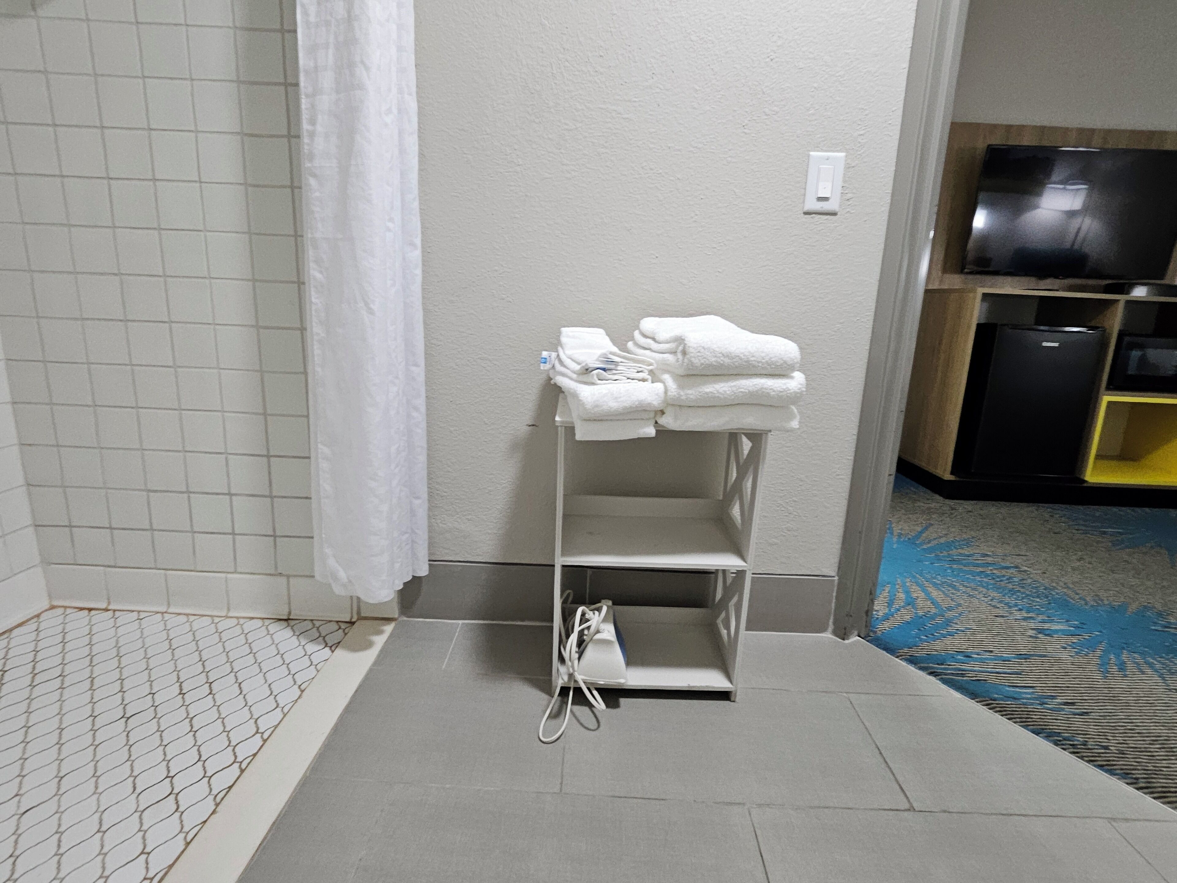 Un baño con ducha, un perchero con toallas dobladas, un enchufe y un televisor al fondo.