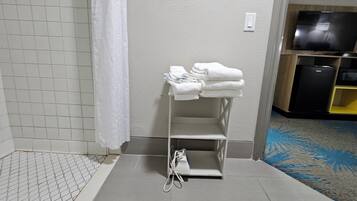 Un baño con ducha, un perchero con toallas dobladas, un enchufe y un televisor al fondo.