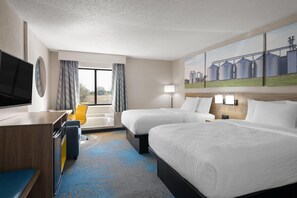 Ein Hotelzimmer mit zwei Betten, einem Schreibtisch, einem Fernseher, einem Gemälde und einem Fenster mit Vorhängen.