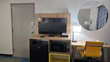 Une chambre d’hôtel équipée d’une télévision, d’un four à micro-ondes, d’un petit réfrigérateur, d’un bureau avec une lampe et d’une chaise.