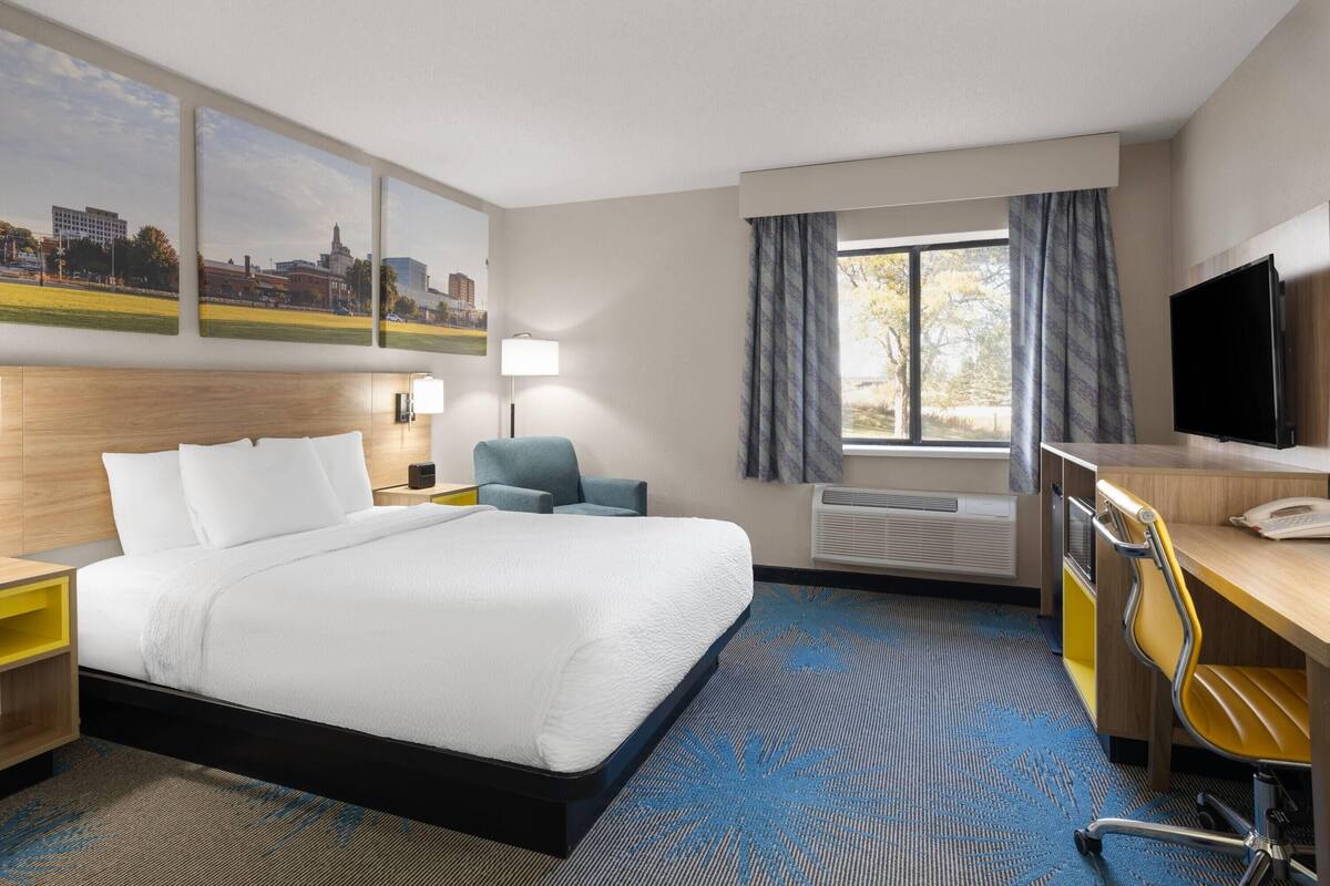 Une chambre d’hôtel avec un grand lit, un bureau avec une chaise, un téléviseur à écran plat et une fenêtre avec des rideaux.