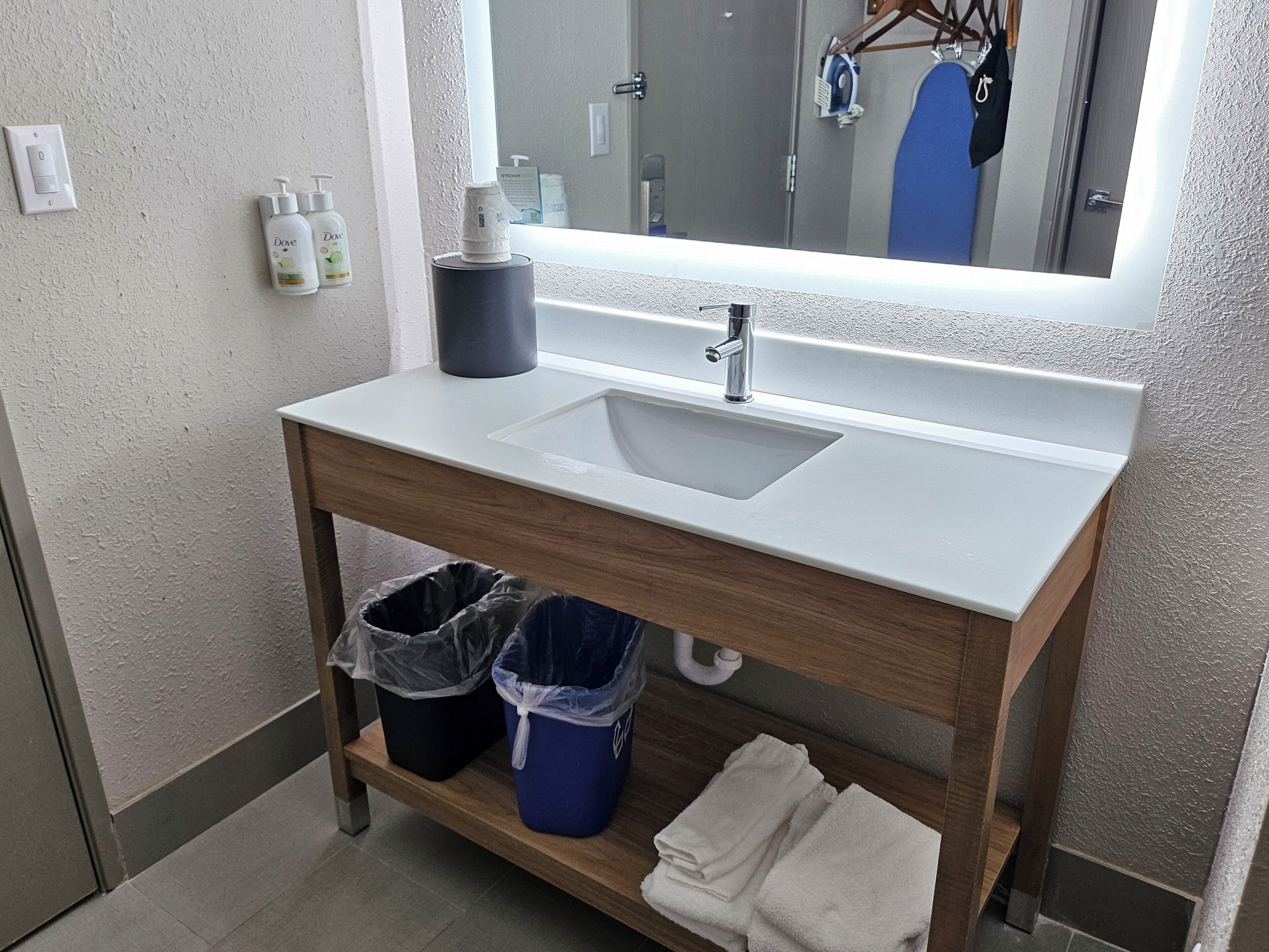 A bathroom with a white sink, wooden vanity, two trash bins, and a mirror above the sink.