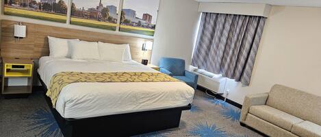 A hotel room with a large bed, a chair, a desk, and a window with curtains.