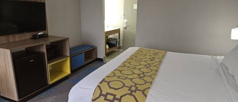 A hotel room with a bed, a TV, a desk, and a storage unit.