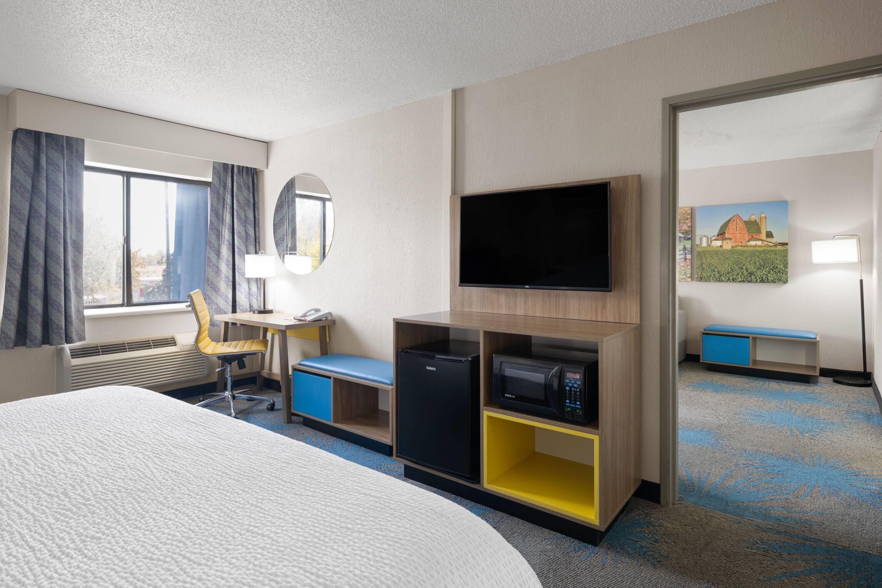 Habitación de hotel con cama, escritorio, silla, televisor, refrigerador y microondas.