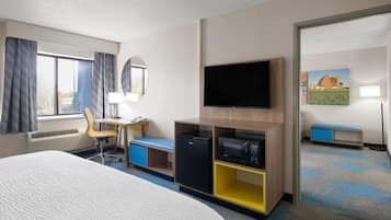 Habitación de hotel con cama, escritorio, silla, televisor, refrigerador y microondas.