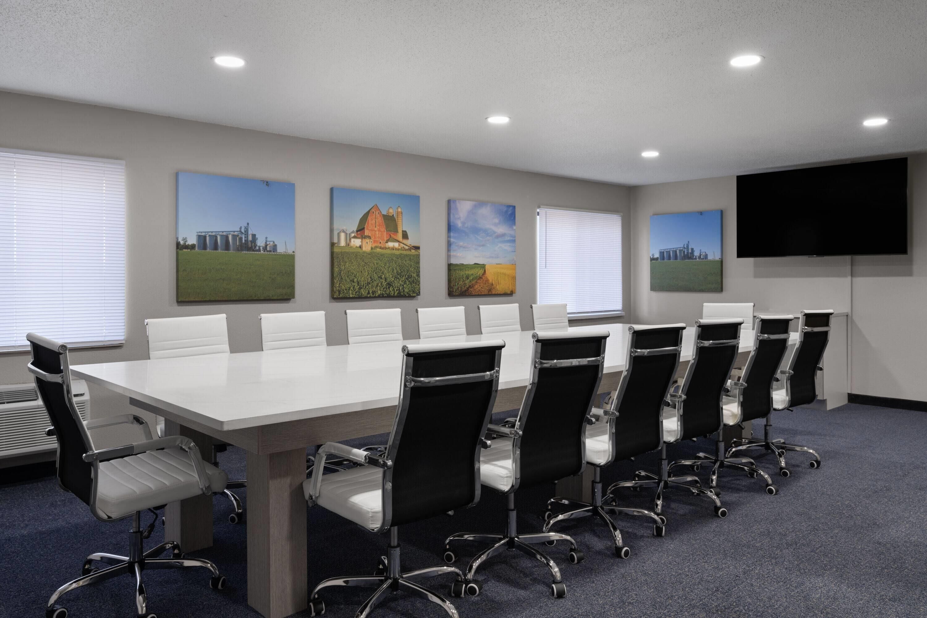 A conference room with a long table, six chairs, and three paintings on the wall.