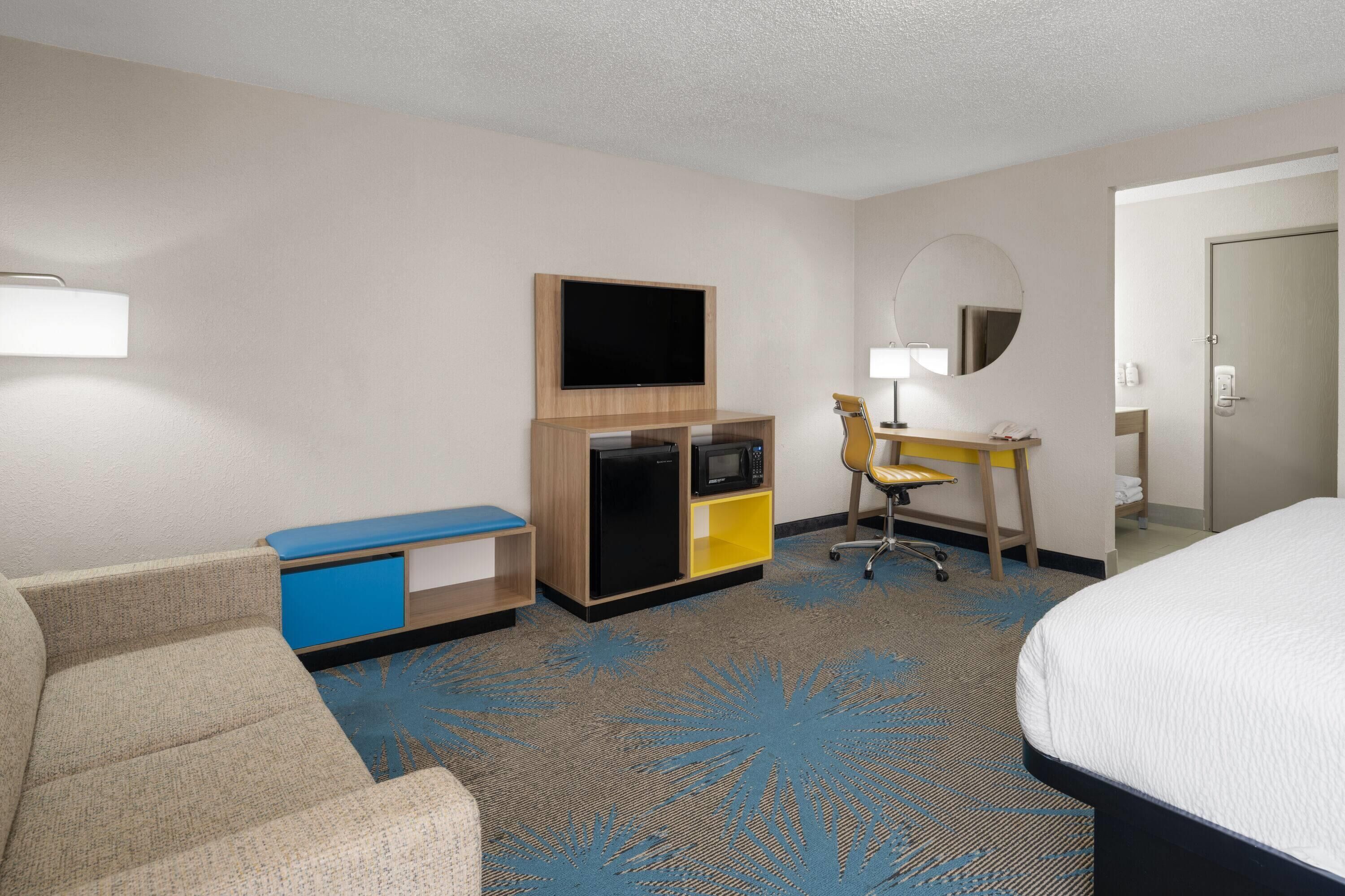 A hotel room with a bed, a desk with a computer, a television, a microwave, and a refrigerator.