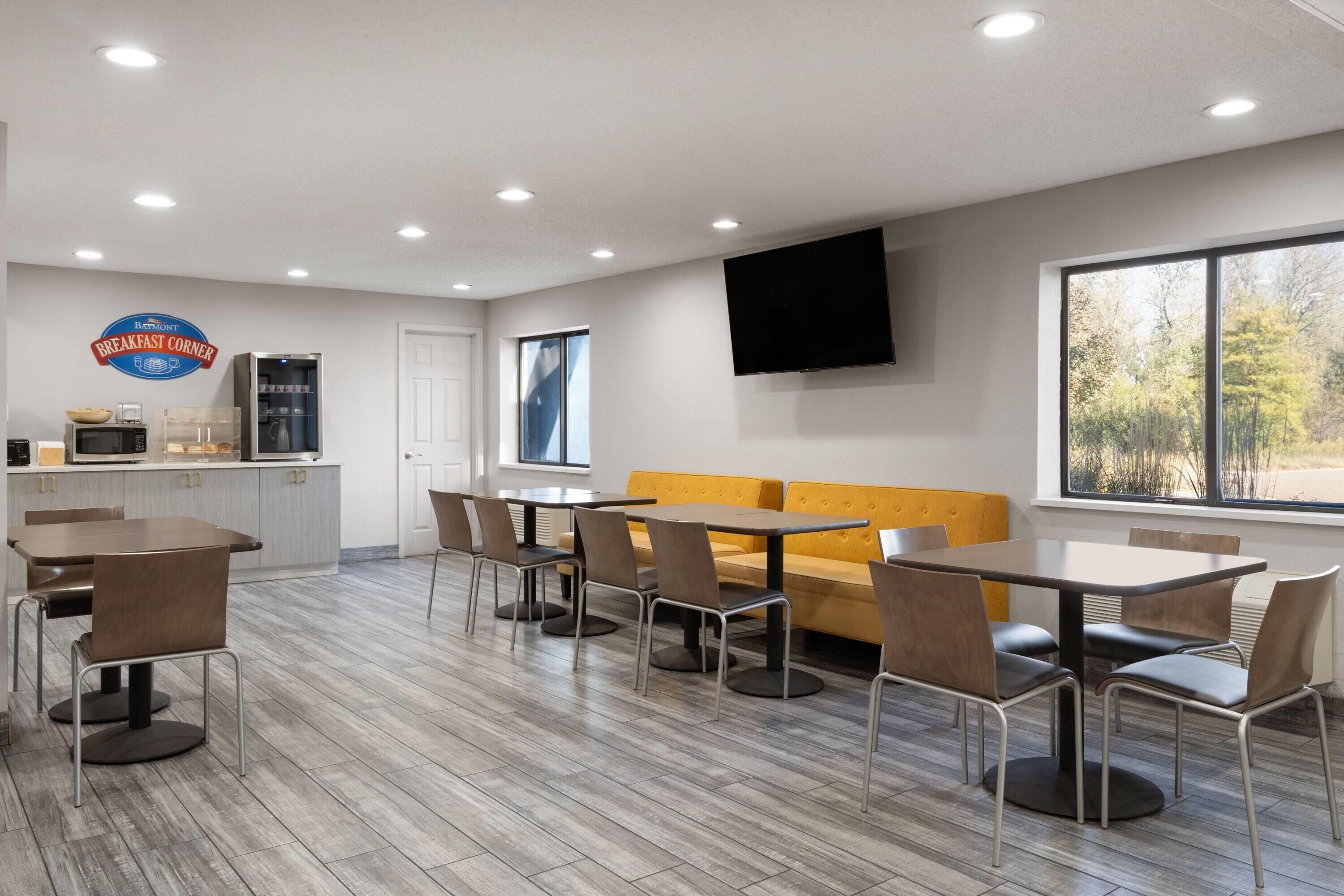 A modern breakfast area with a kitchen, seating, and a large window.