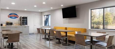 A modern breakfast area with a kitchen, seating, and a large window.