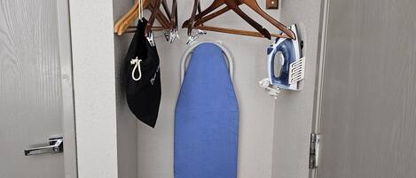 A closet with a hanging rack, a blue ironing board, and a black bag.