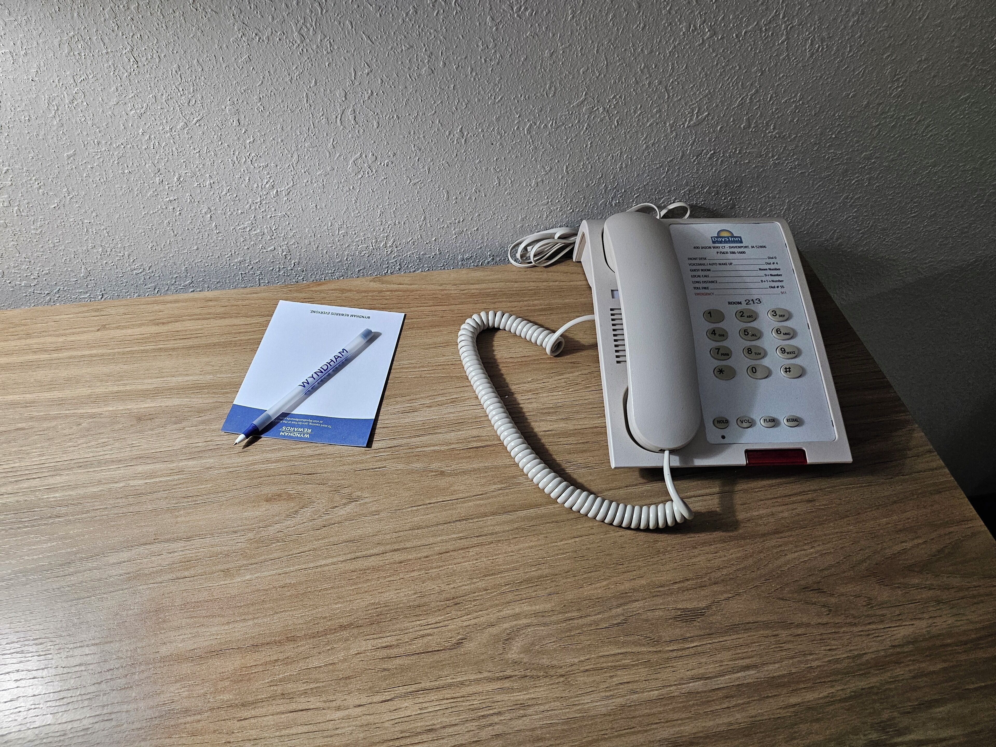 Un téléphone d’hôtel posé sur une table en bois, avec un stylo et une carte de visite.