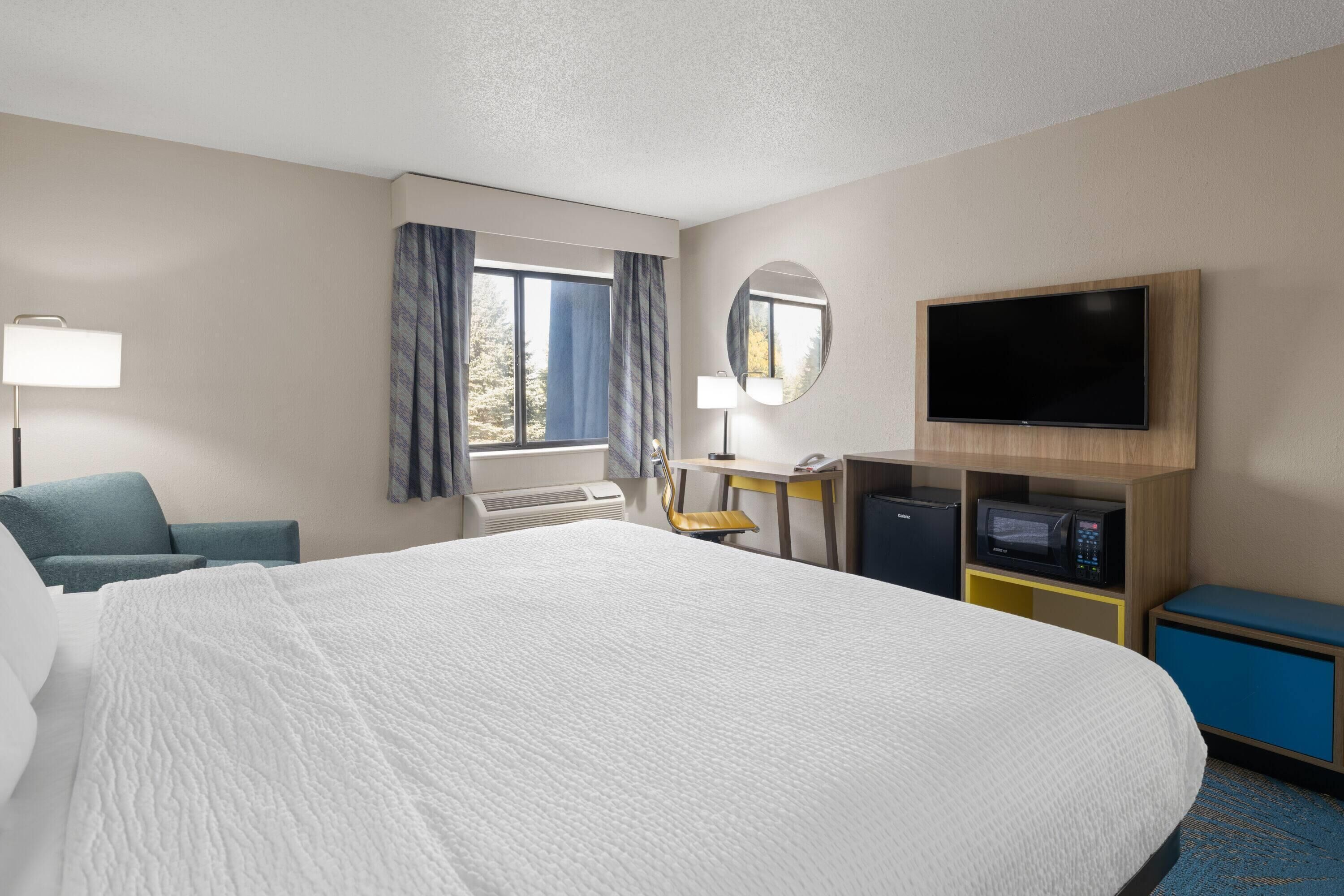 A hotel room with a large bed, a desk, a chair, a television, and a microwave.