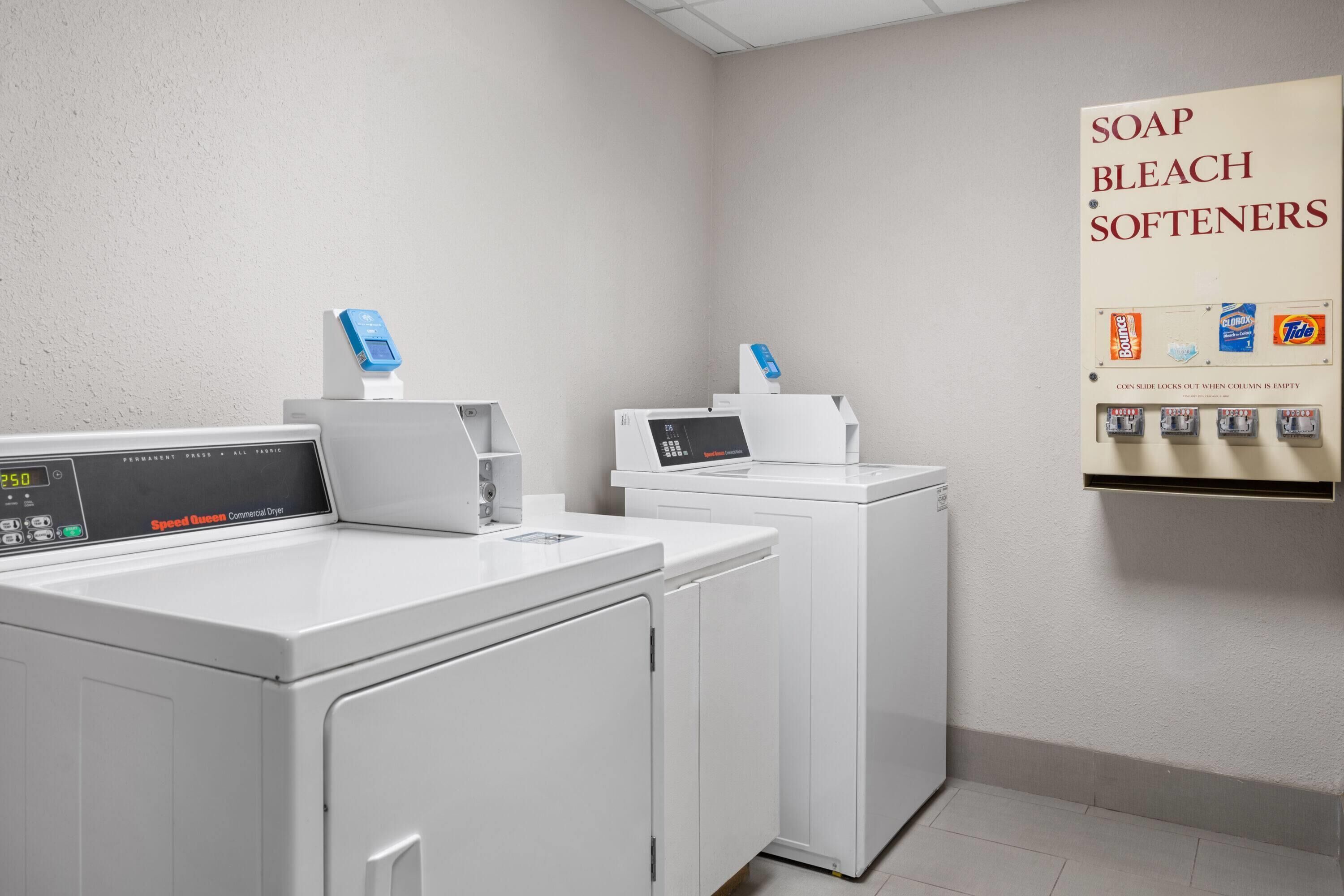 A laundry area with two washing machines and a wall-mounted dispenser for soap, bleach, and softeners.