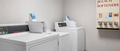 A laundry area with two washing machines and a wall-mounted dispenser for soap, bleach, and softeners.