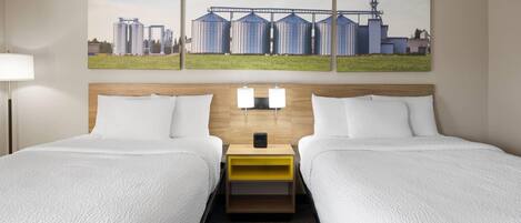 Habitación de hotel con dos camas, un cabecero de madera, una mesita de noche con lámparas y un cuadro de gran tamaño con temática industrial sobre las camas.