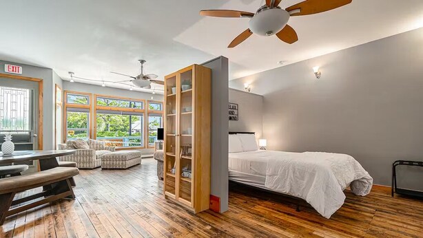 Une chambre avec un lit, une armoire en bois, un ventilateur de plafond et une vue sur la verdure.