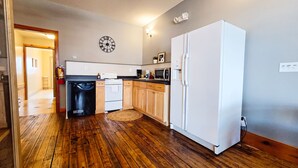 Une cuisine avec un plancher en bois, un réfrigérateur blanc, un lave-vaisselle et une horloge au mur.