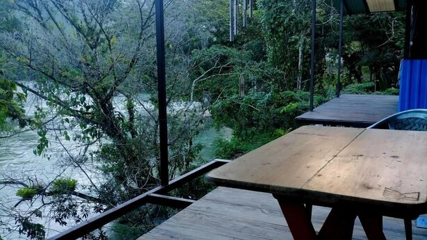 A wooden deck with a picnic table and chairs, overlooking a body of water and surrounded by trees. - Room in Cabin - Rafting Hut by The River (San Agustin Lanquin)