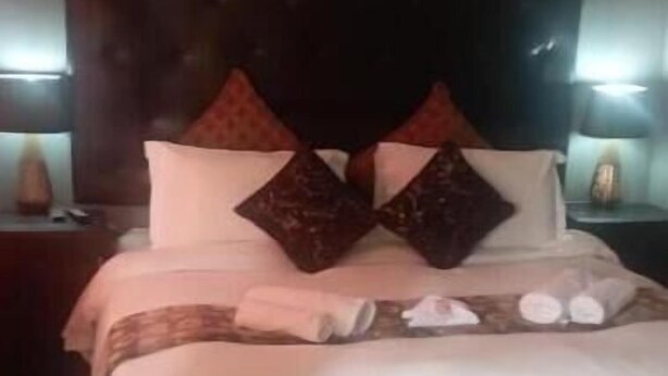 Una cama bien hecha con almohadas y una manta, un cabecero, mesitas de noche con lámparas y un cuadro en la pared.