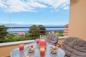 A balcony with a table set for two, glasses of a pink drink, and bowls of nuts and dried fruits.