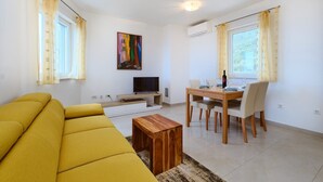 A living room with a sofa, TV, dining table, chairs, and a painting on the wall.
