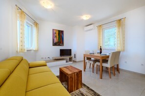 Un salon comprenant un canapé, un téléviseur, une table à manger, des chaises et un tableau accroché au mur.