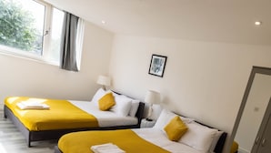 Una habitación de hotel con dos camas, cada una con cubrecama amarillo y almohadas blancas, una lámpara de noche y un cuadro en la pared.