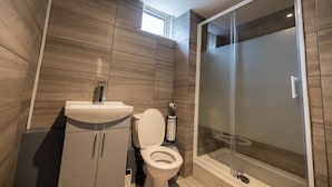 Un baño moderno con inodoro, lavamanos y ducha con mampara de vidrio.