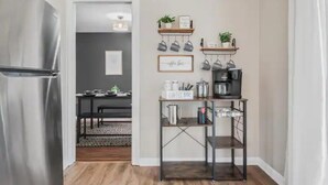 Una cocina con refrigerador de acero inoxidable, una barra de café y estantes con utensilios de cocina y plantas.