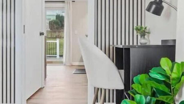Un interior moderno con piso de madera, una silla blanca, un escritorio negro y una planta en maceta.